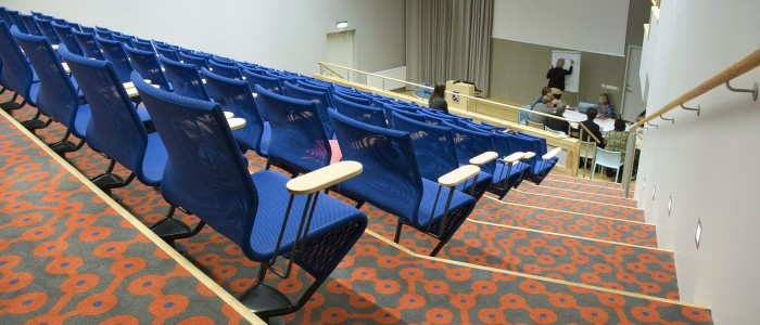 auditorijas iebūvētās sēdvietu mēbeles ar galdiņiem